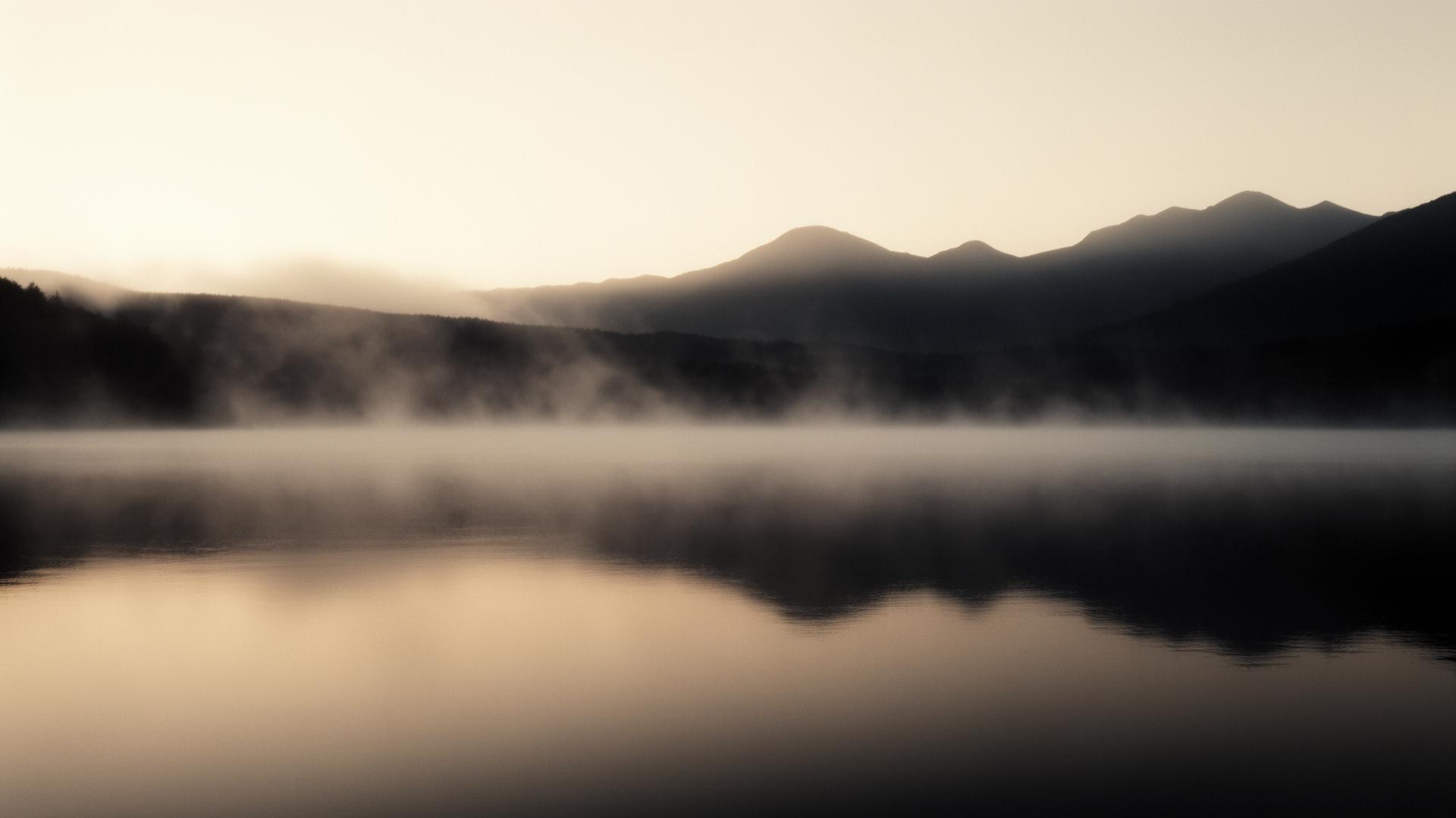 Mist drifting over a still lake at dawn